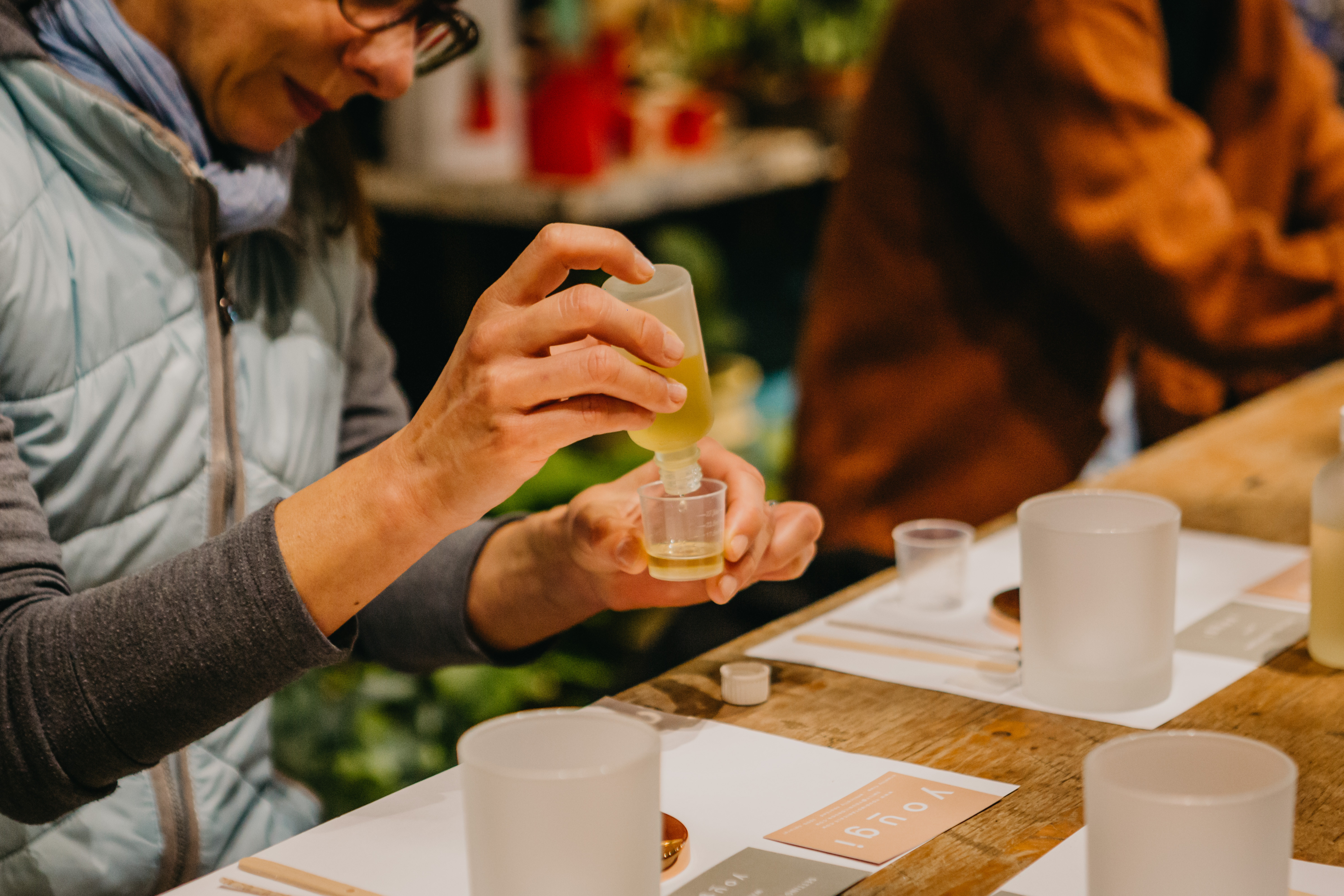 A woman wearing glasses decants essential oils into a small glass container